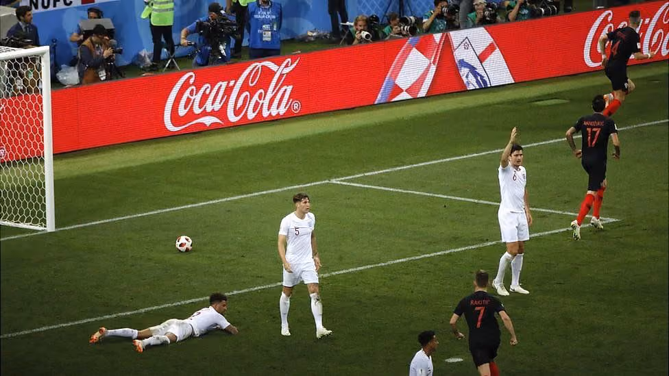 Soccer players near goalpost with one raising hand, others in white and black jerseys on the field.