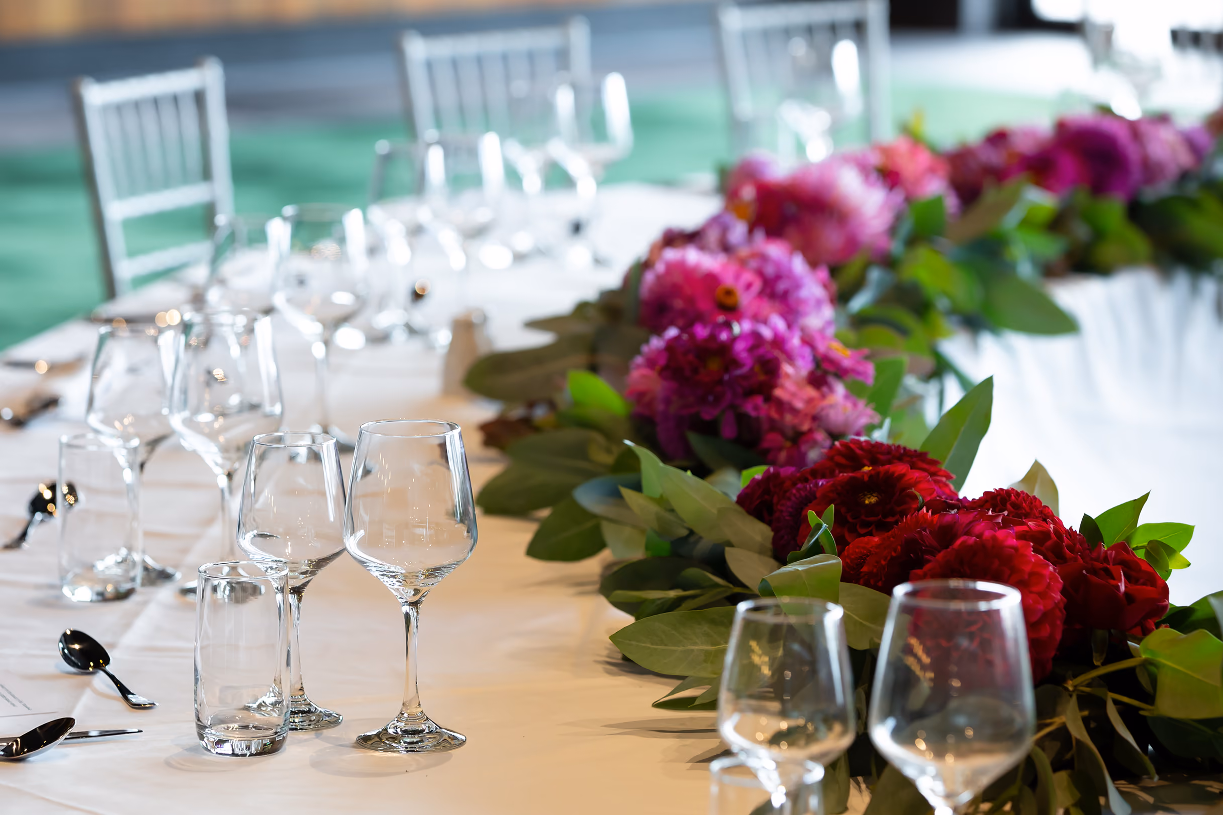Table set with empty wine glasses and floral centerpiece with red and purple flowers and green leaves.