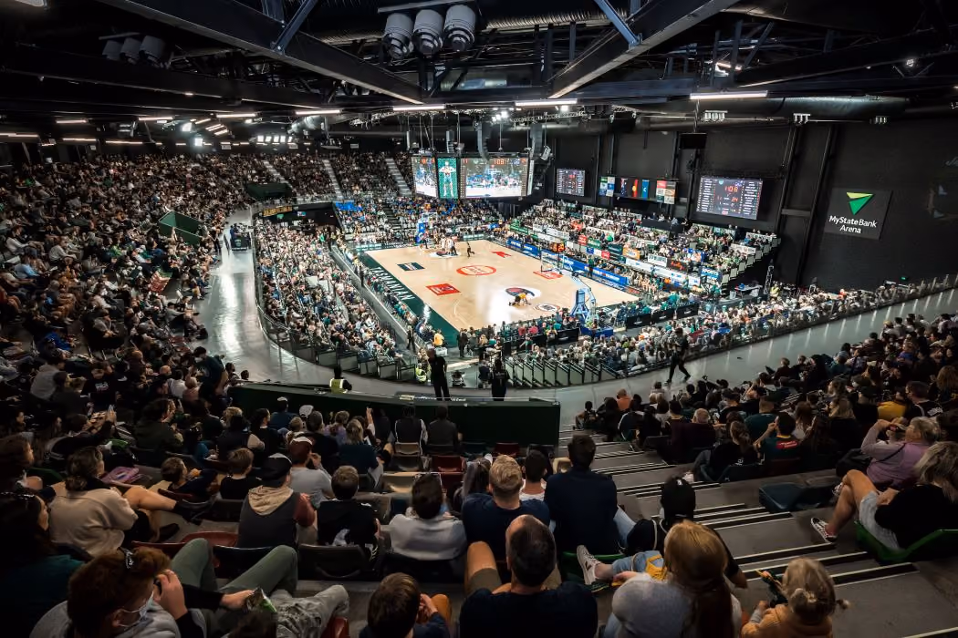 Packed indoor arena with spectators watching a basketball game on a hardwood court.