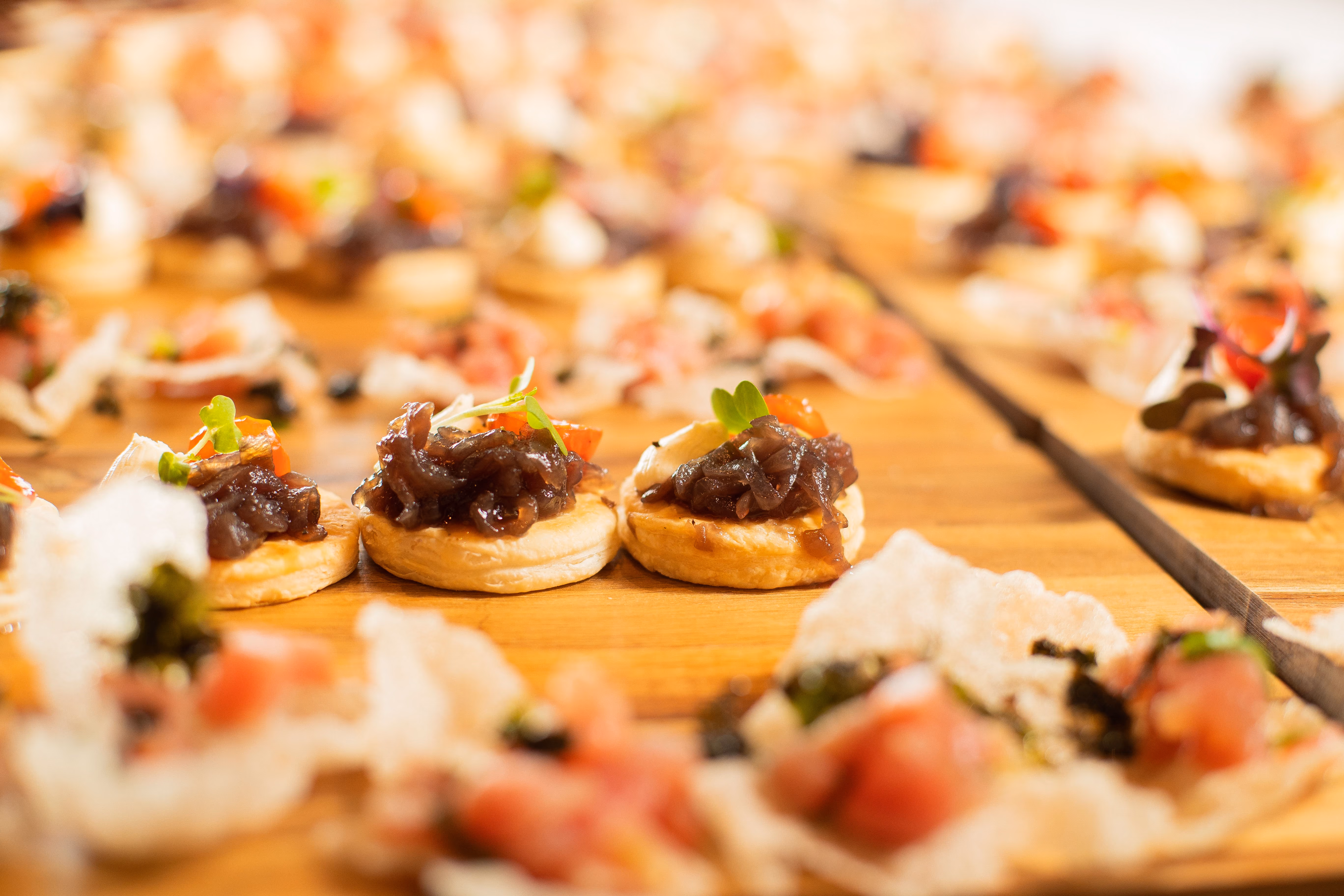 Close-up of small appetizers with caramelized onions and herbs on a wooden board.