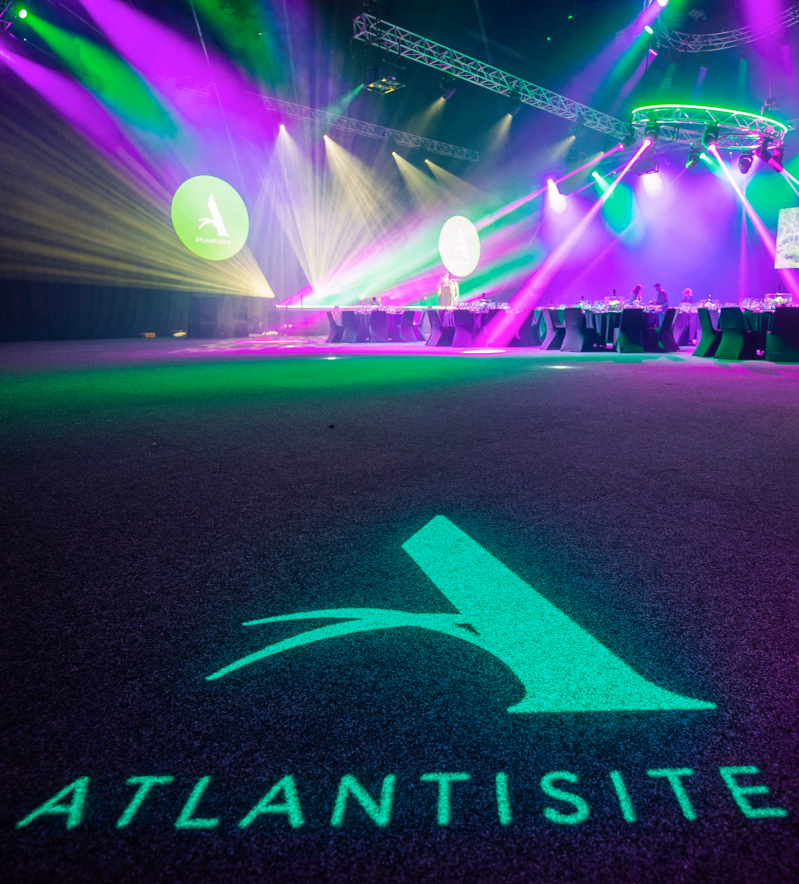 Event venue with purple and green lights and the Atlantisite logo projected on carpet and walls.