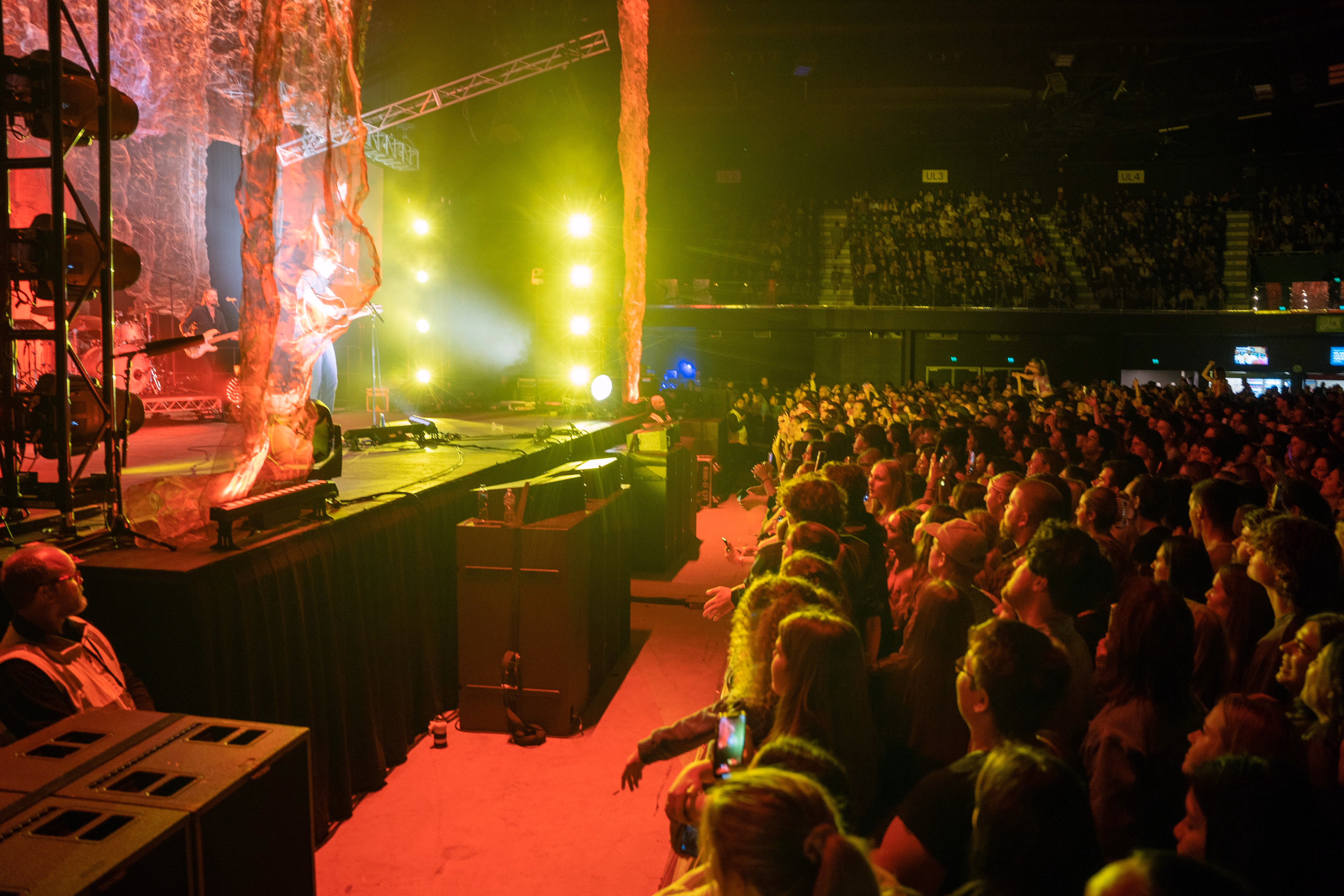 Large crowd watching a live music performance with yellow stage lights and a visible security guard