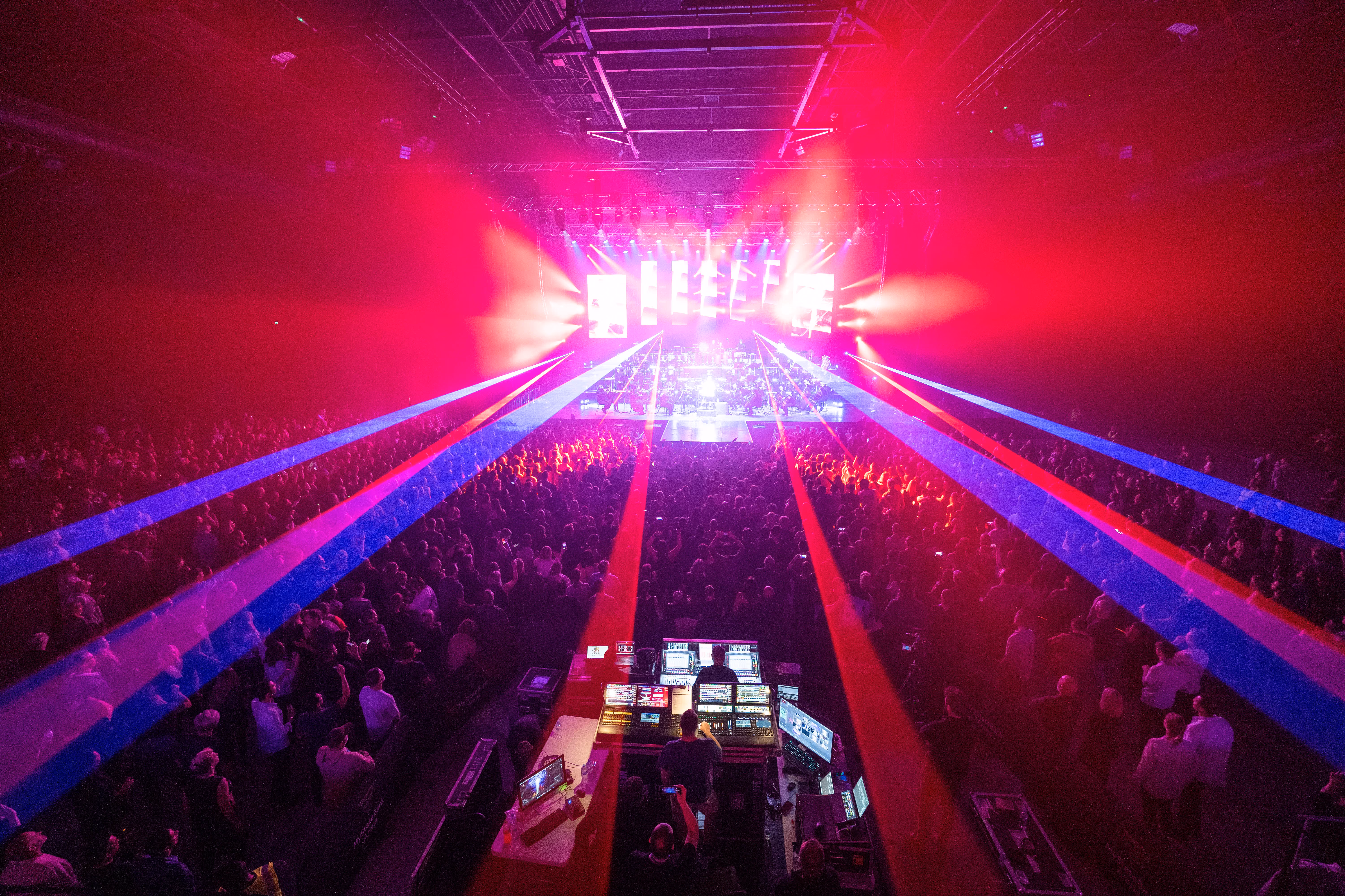 Large crowd at a concert with bright red and blue stage lights shining over the audience.