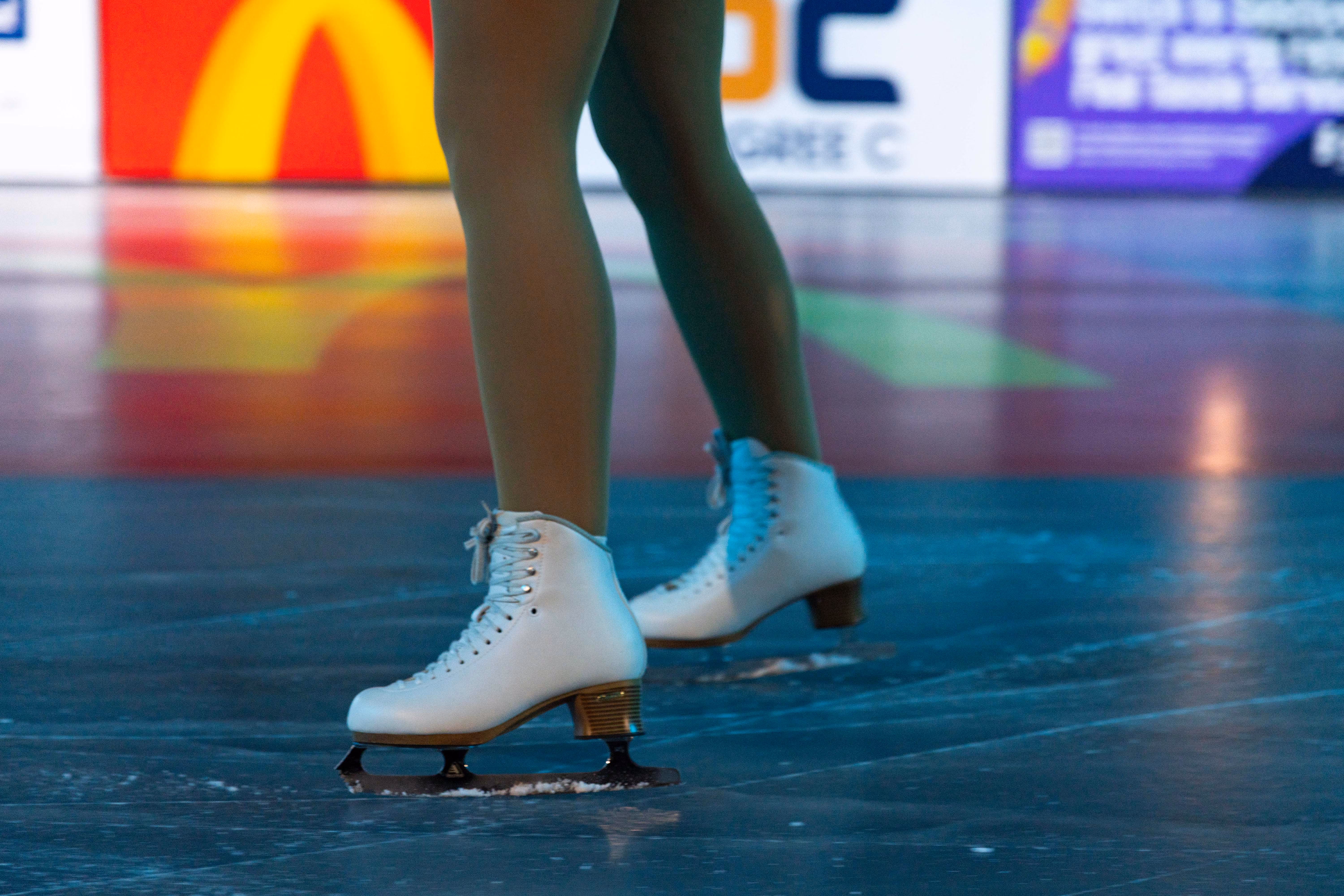 Close-up of a figure skater's legs wearing white ice skates on an ice rink surface.