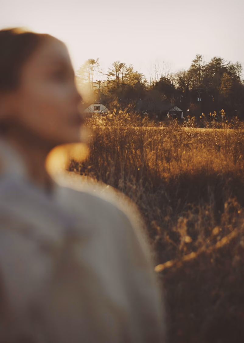 Blurred close-up of a woman with a field and trees in the background at golden hour light.