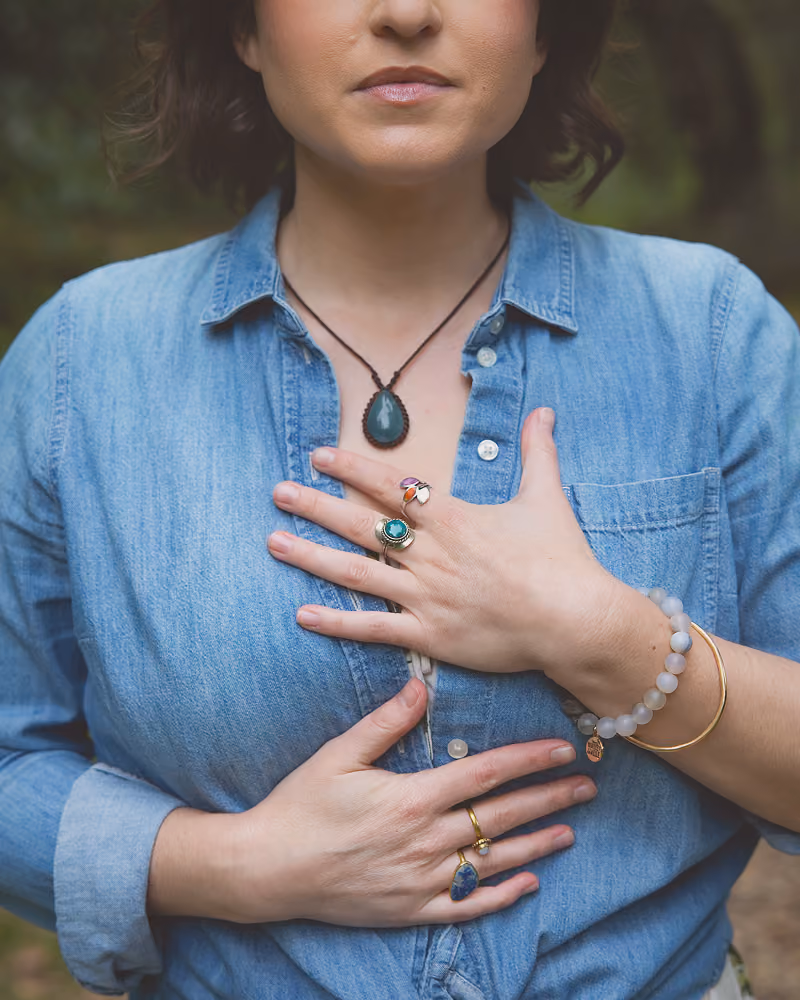 Leah Hoffman in denim shirt with rings, bracelets, and a pendant necklace, hands near her chest.