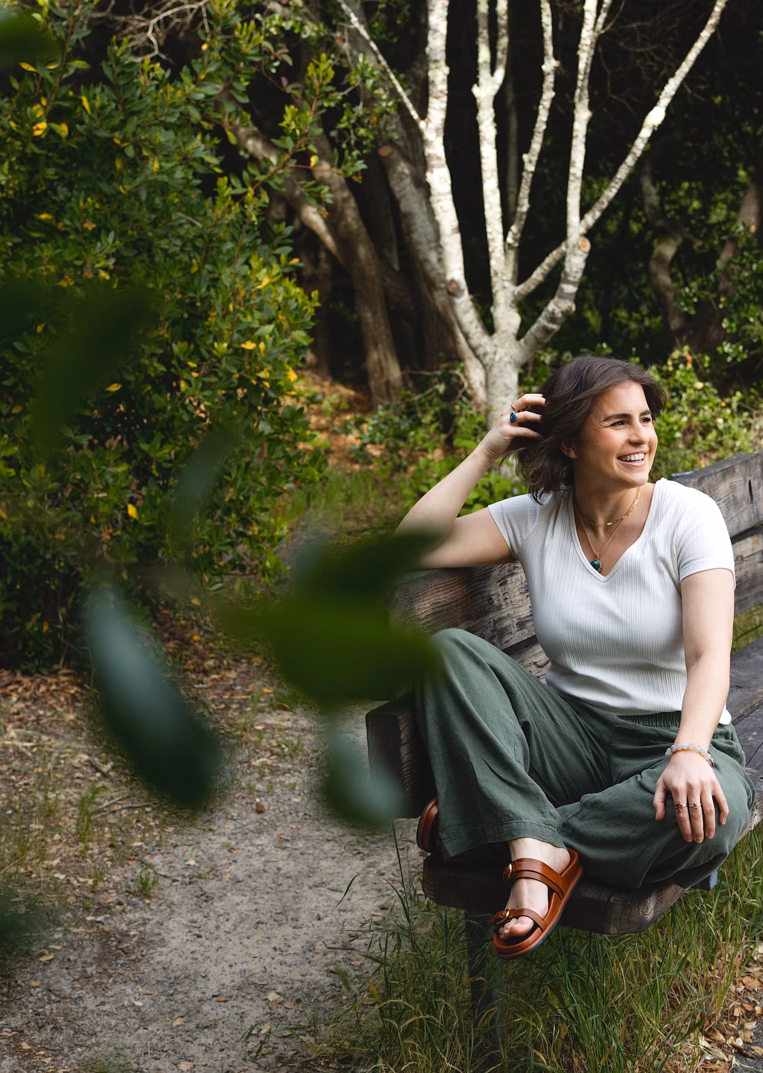 Leah Hoffman sitting on a wooden bench outdoors surrounded by greenery and trees.