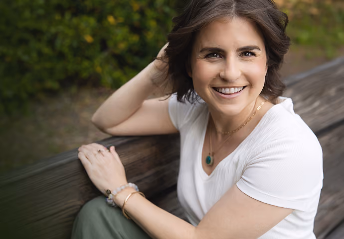 Leah Hoffman sitting on a wooden bench outdoors, wearing white top.