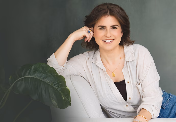 Leah Hoffman sitting on a light sofa against a muted green background.