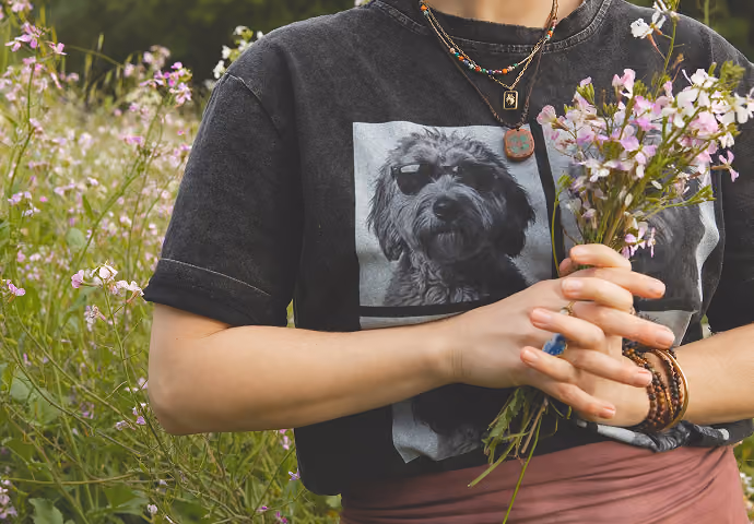 Person wearing dog print shirt and bracelets holding a bouquet of pink and white flowers.