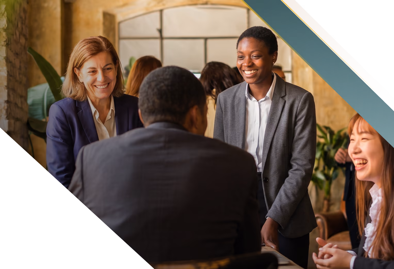 A diverse group of four business professionals in a casual meeting, smiling and engaging in conversation around a table in a warmly lit room.