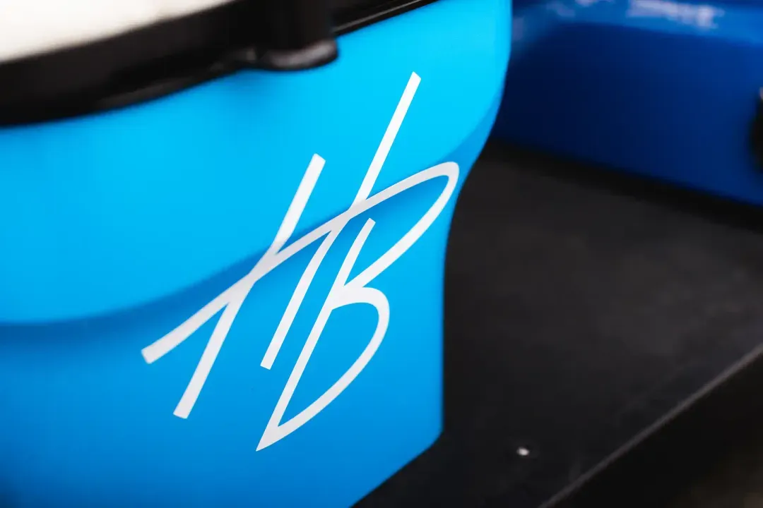 Close-up of a white stylized 'HB' logo on a bright blue surface, likely part of machinery or equipment.