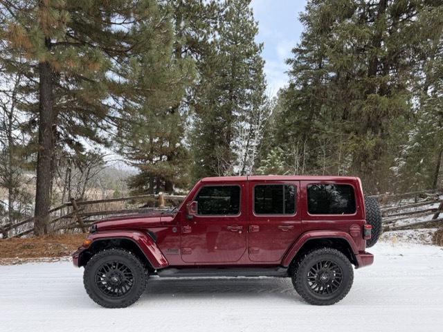 Red Jeep Wrangler on a snowy road among pine trees