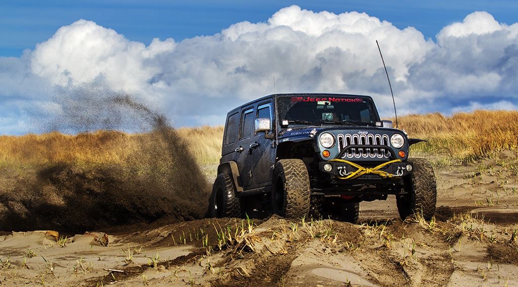 Black Jeep kicking up sand on coastal dunes