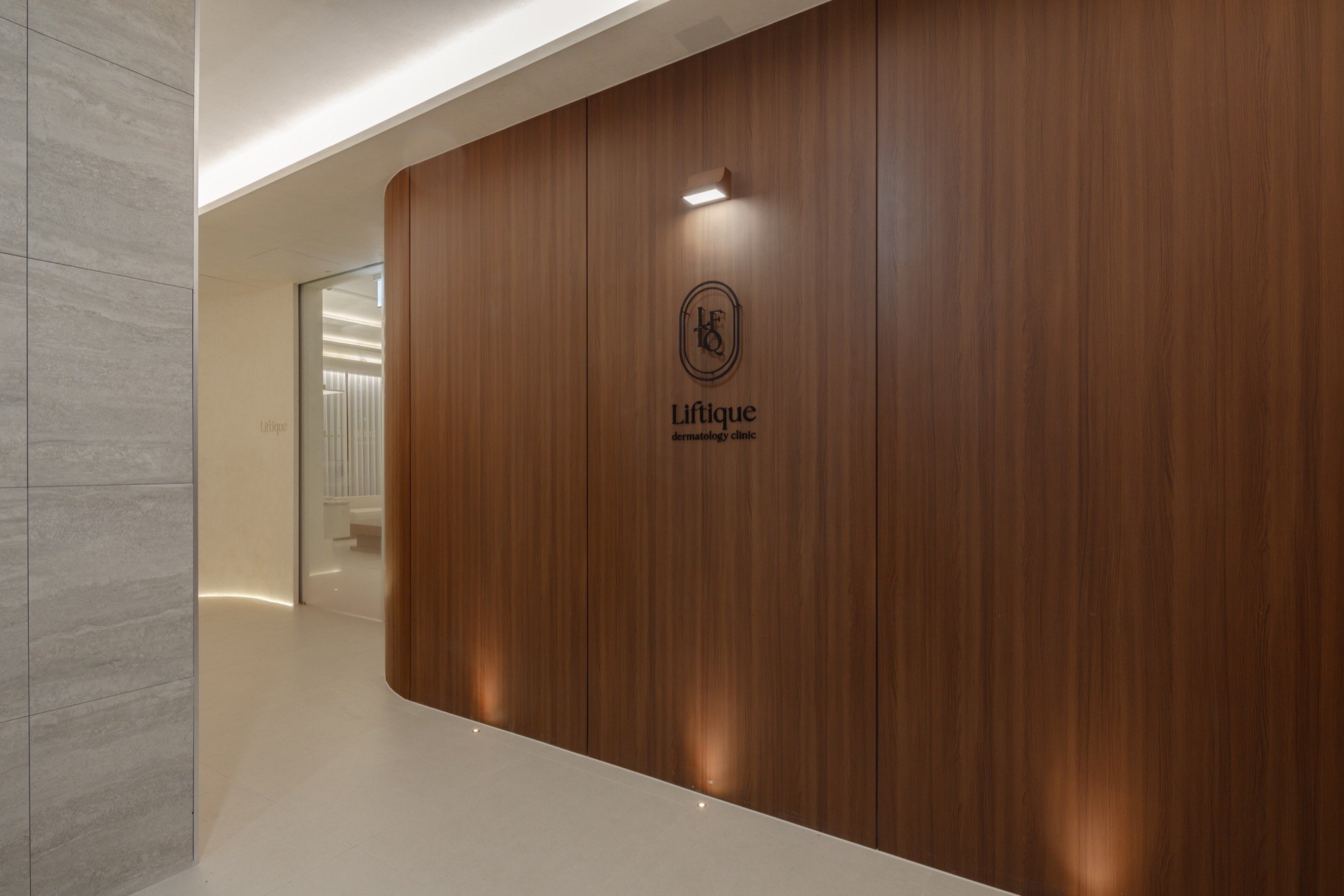 Liftique Dermatology Clinic entrance with a curved wood wall and clinic logo