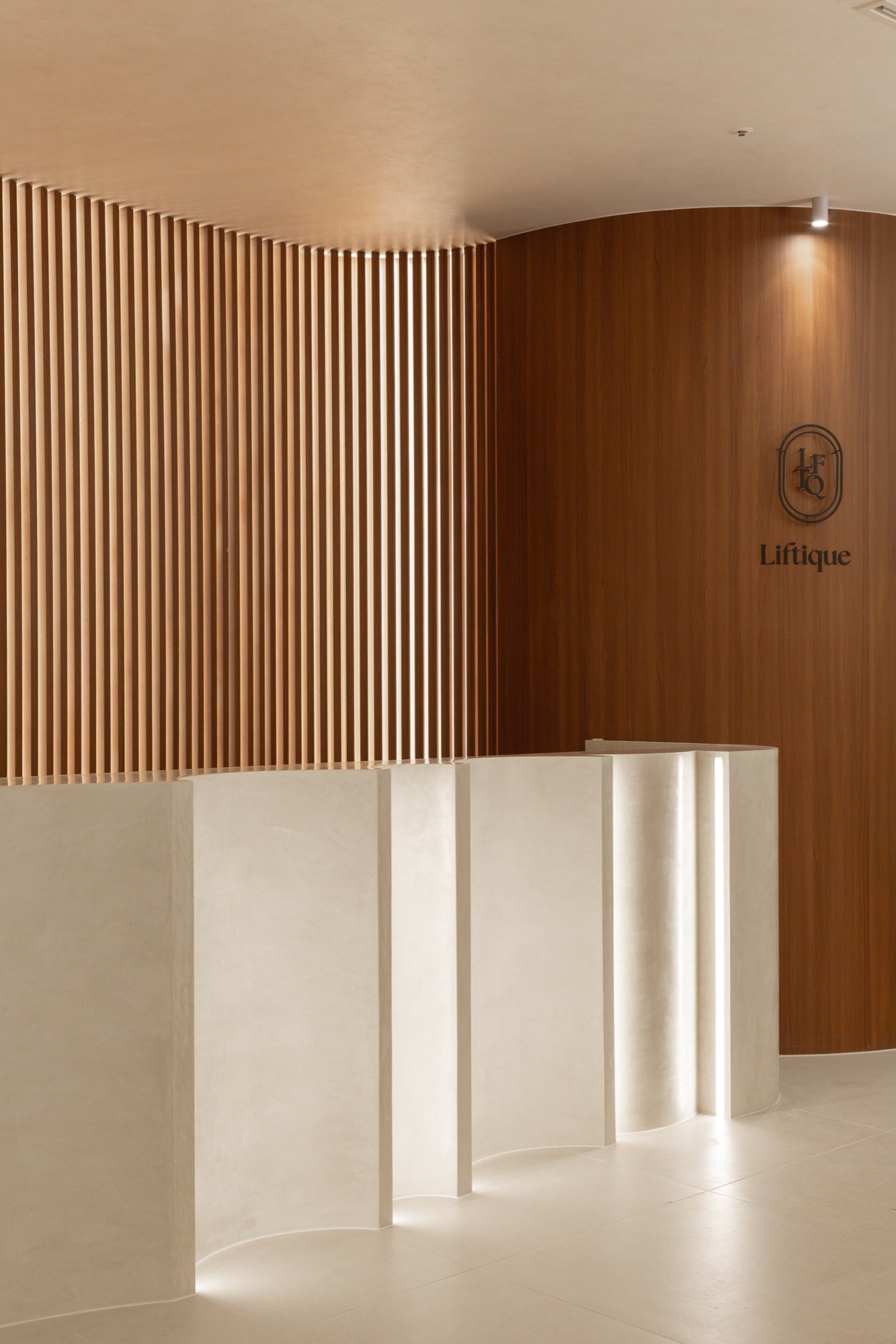 Liftique Dermatology Clinic reception desk with curved wood walls and clinic logo