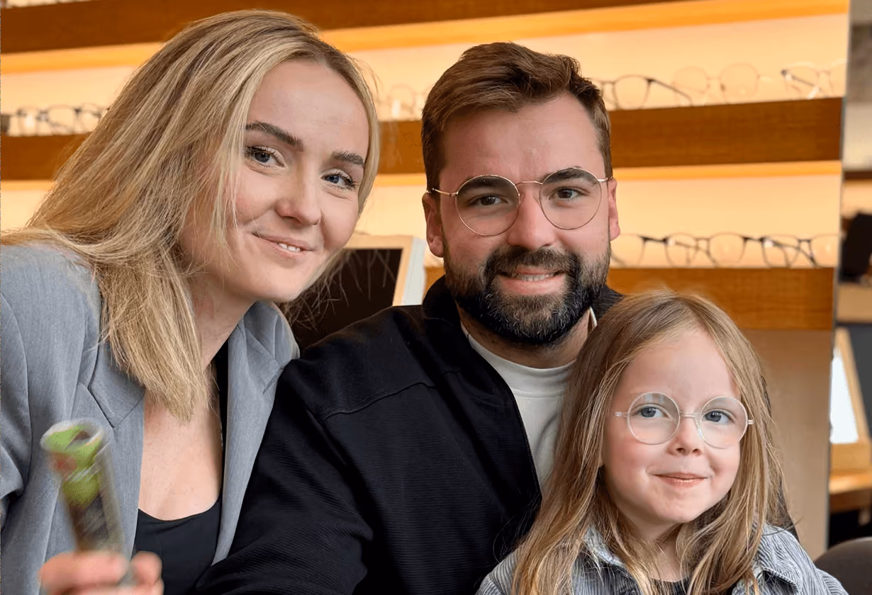 Fröhliche Familie mit Brille im Geschäft, Erwachsene lächeln, Kind mit blonden Haaren und Brille.