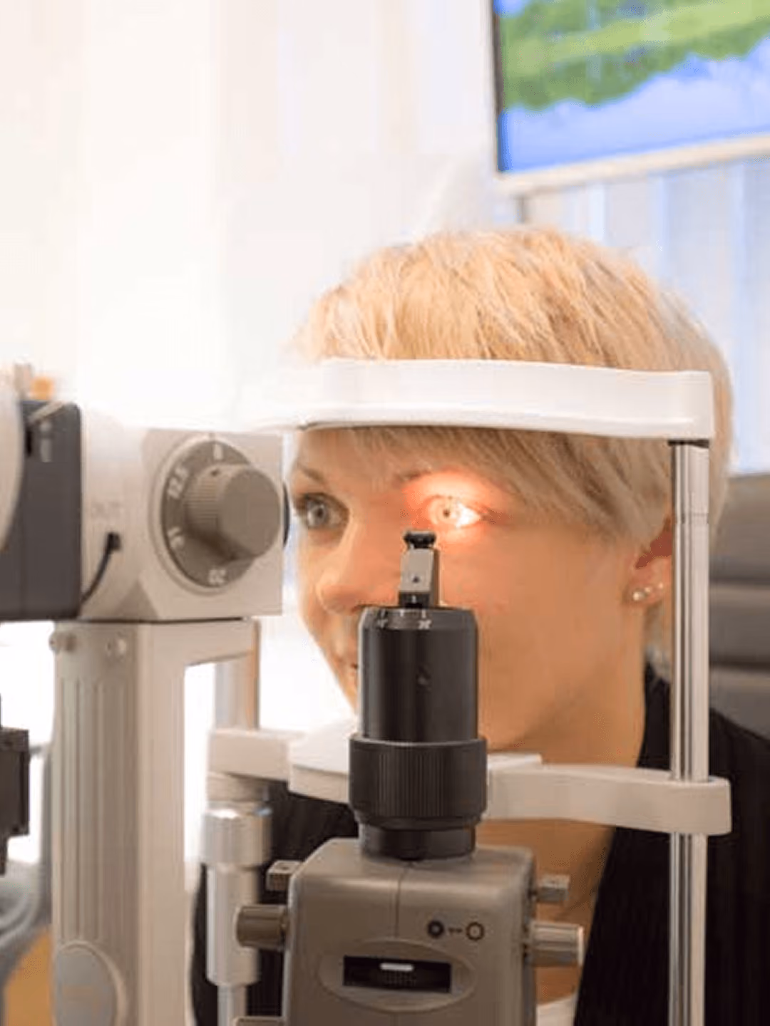 Frau beim Augenarzt, Augenuntersuchung mit Spaltlampe, blondes Haar, Fokus auf Augenuntersuchung.