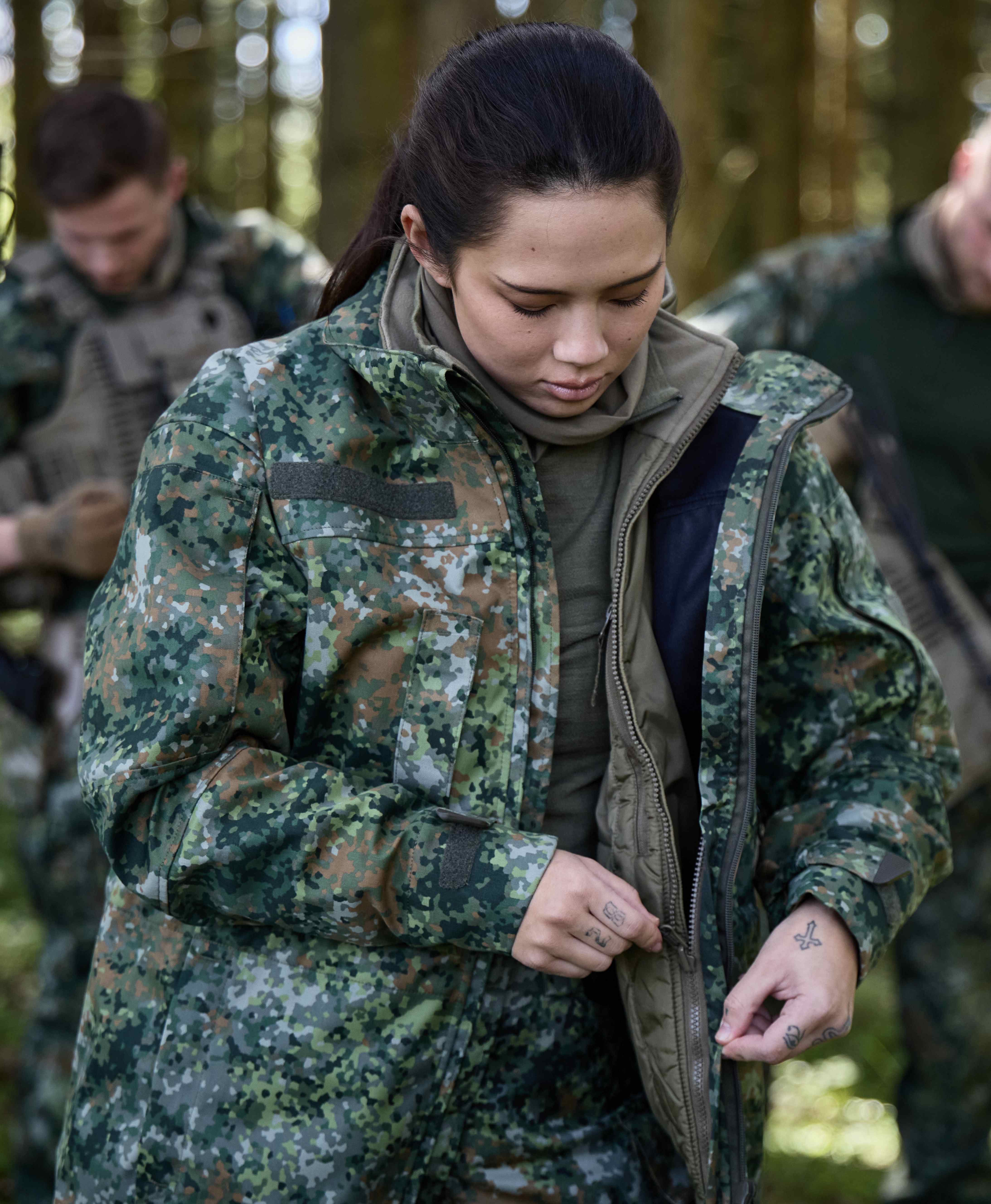 Einsatzkraft in mehrschichtiger Tarnbekleidung bereitet ihre Ausrüstung im Wald vor.