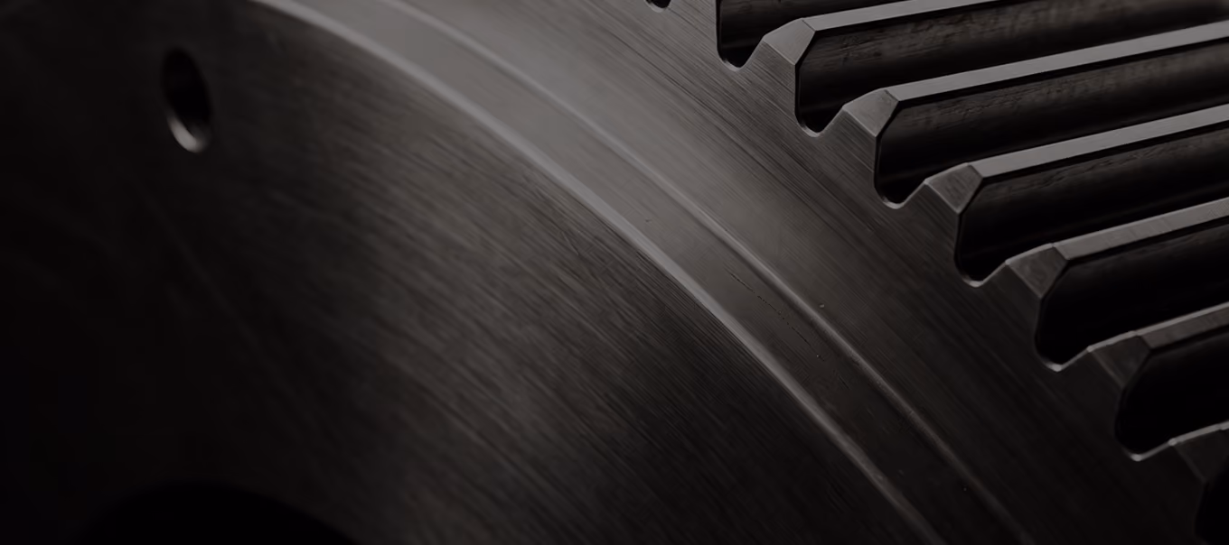 Close-up view of a large metal gear with textured surface and evenly spaced teeth on a dark background.
