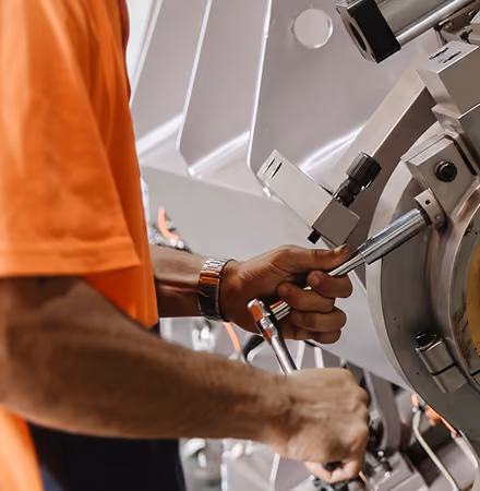 Person in an orange shirt operating a metal machine using two levers in an industrial setting.