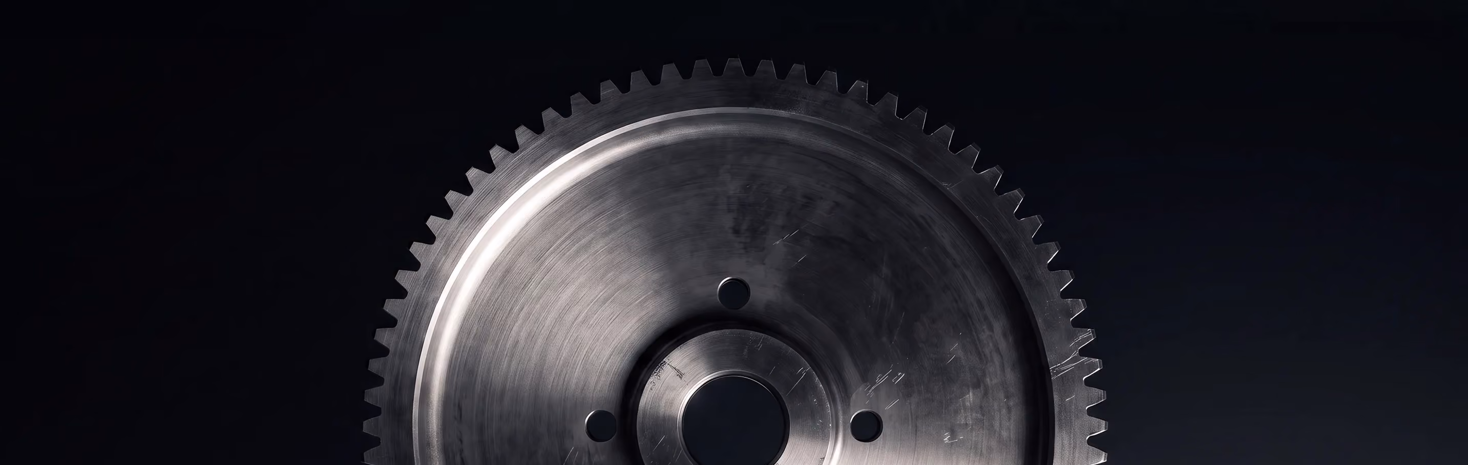Close-up of a metallic gear wheel with evenly spaced teeth around the edge against a dark background.