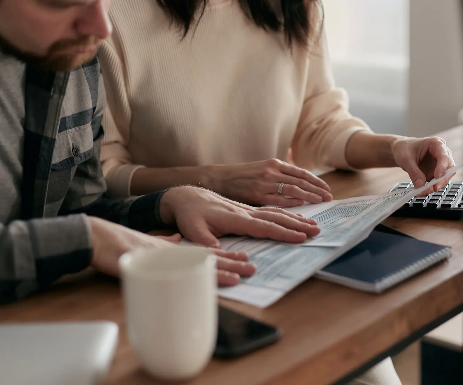 Un homme et une femme examinant des documents financiers sur une table en bois avec un clavier et une tasse de café.