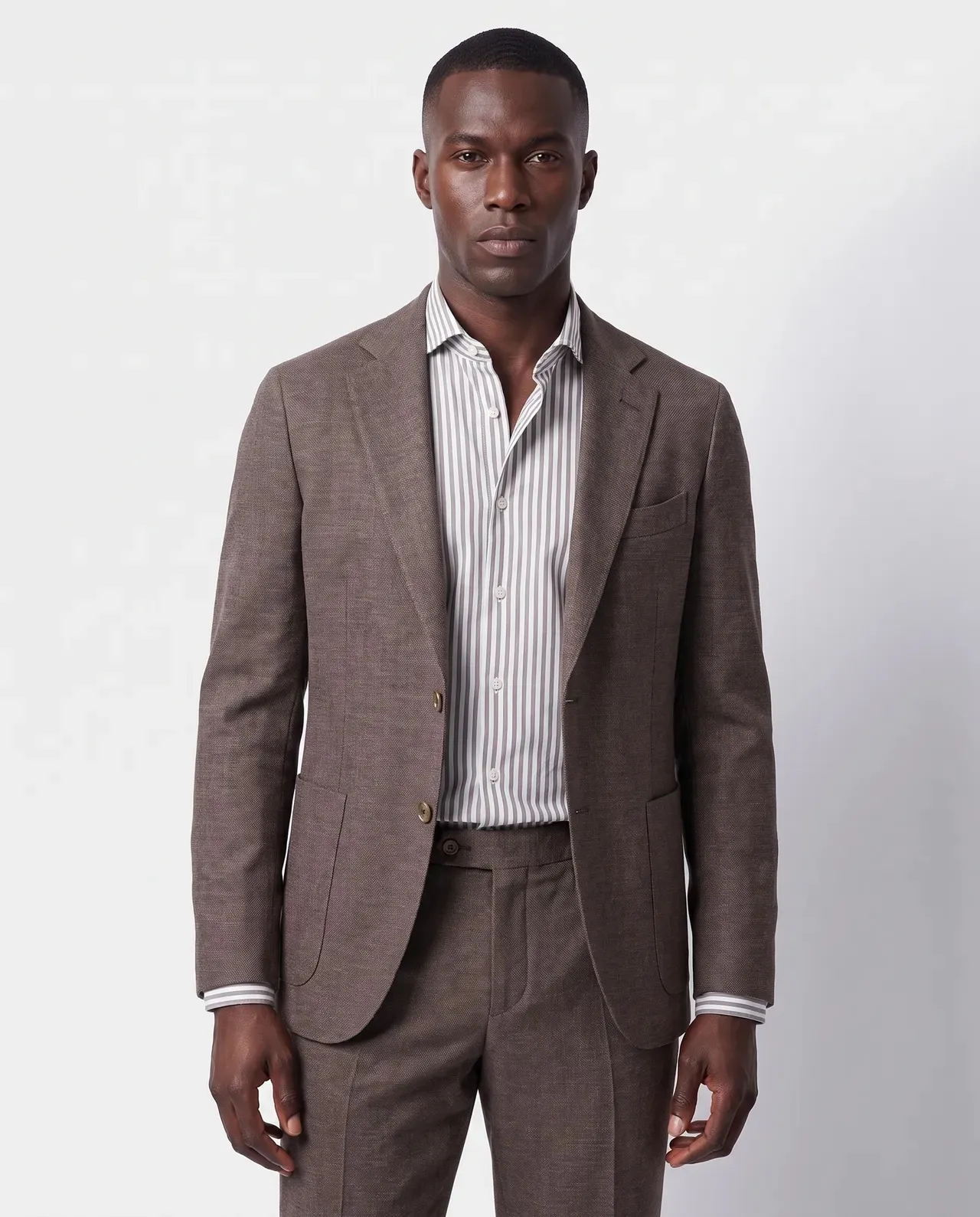 On-model productfoto: man in een bruin pak met een wit overhemd met dunne grijze strepen, driekwart in beeld