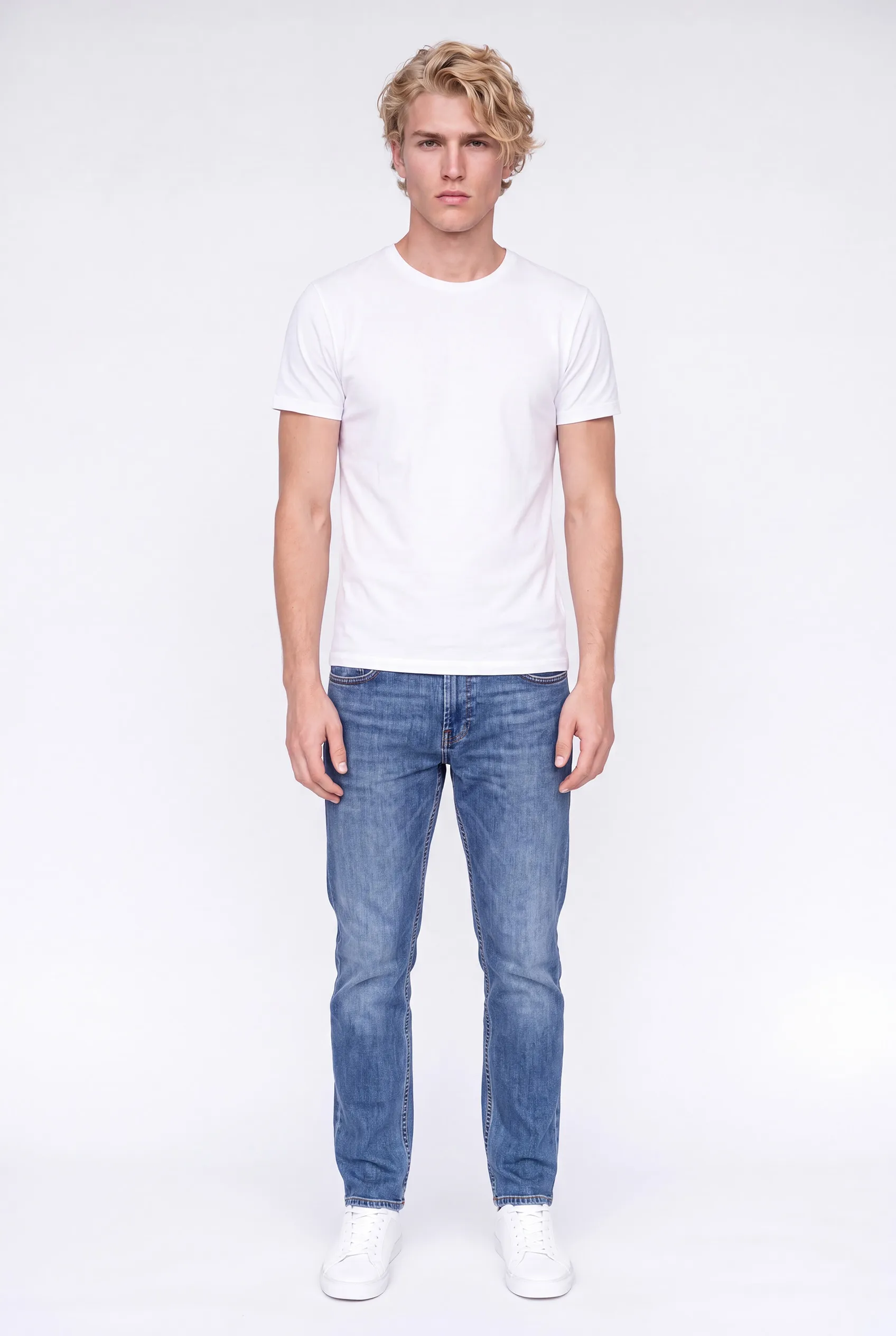Merkmodel Finn ten voeten uit: jonge man met blond krullend haar in een wit T-shirt, spijkerbroek en witte sneakers