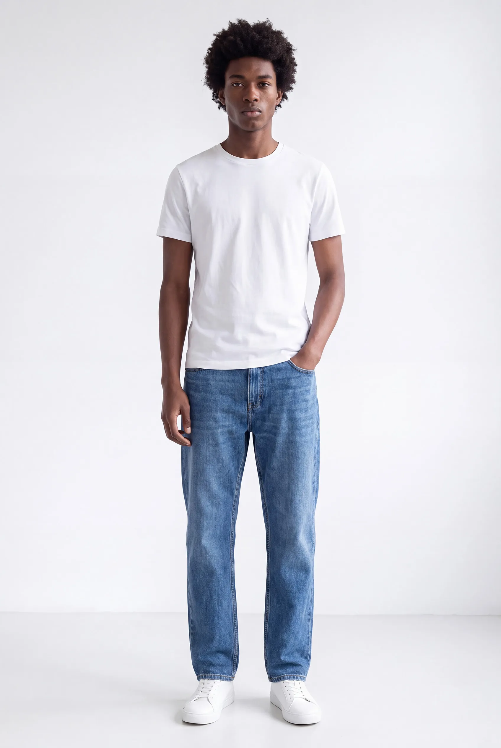 Merkmodel Marcus ten voeten uit: jonge man in een wit T-shirt, spijkerbroek en witte sneakers, tegen een witte achtergrond