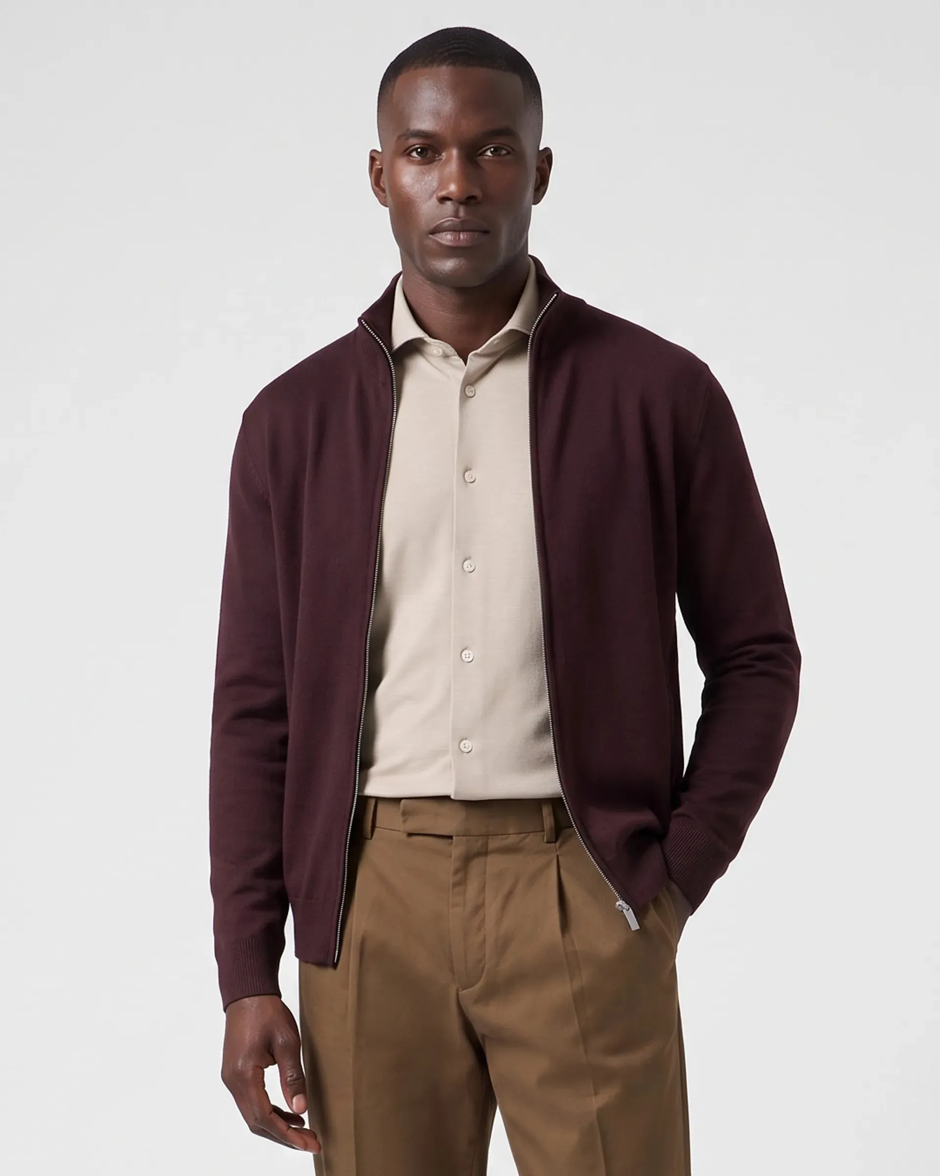On-model productfoto: man in een donkerrood vest met rits over een beige overhemd en een bruine broek
