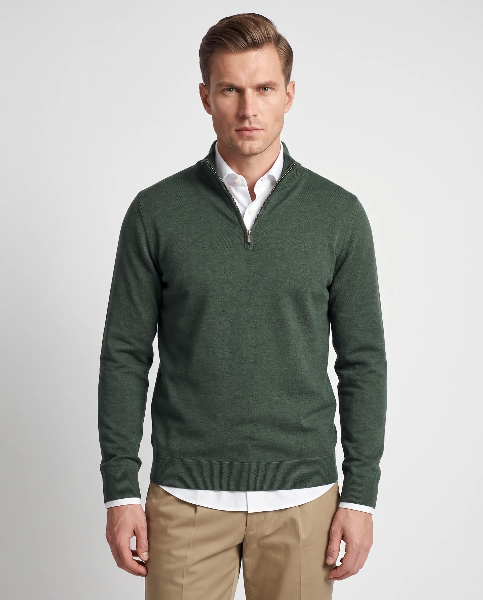 Man wearing a dark green quarter-zip sweater over a white button-down shirt and beige pants, standing against a plain light gray background.