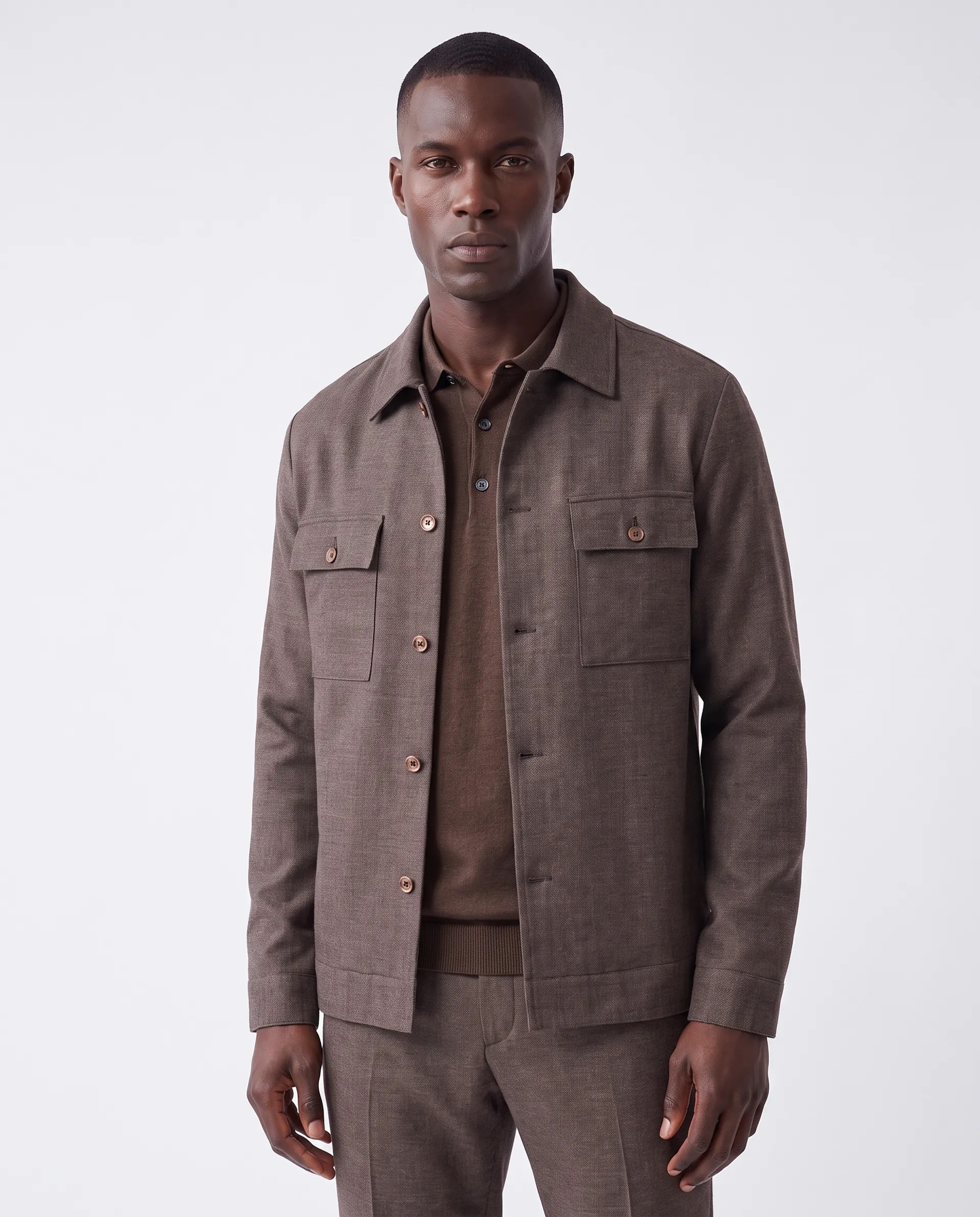 Man wearing a brown button-up jacket over a brown collared shirt and matching brown pants against a plain white background.