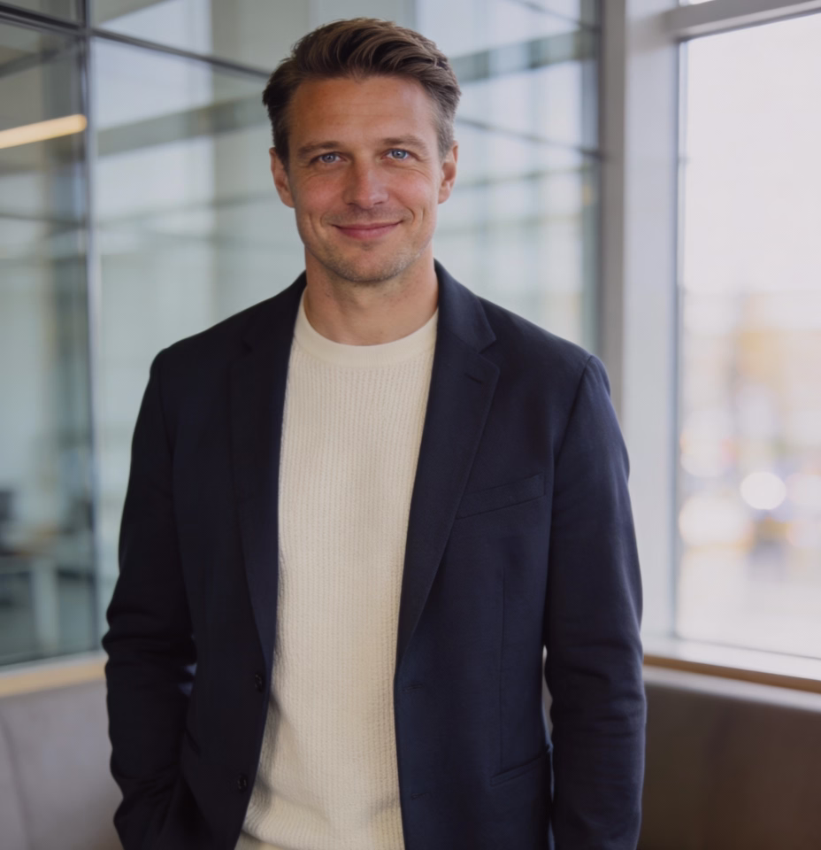 Man in a navy blazer smiling by a window