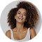 Smiling woman with curly hair wearing a white tank top and gold necklace against a gray background.