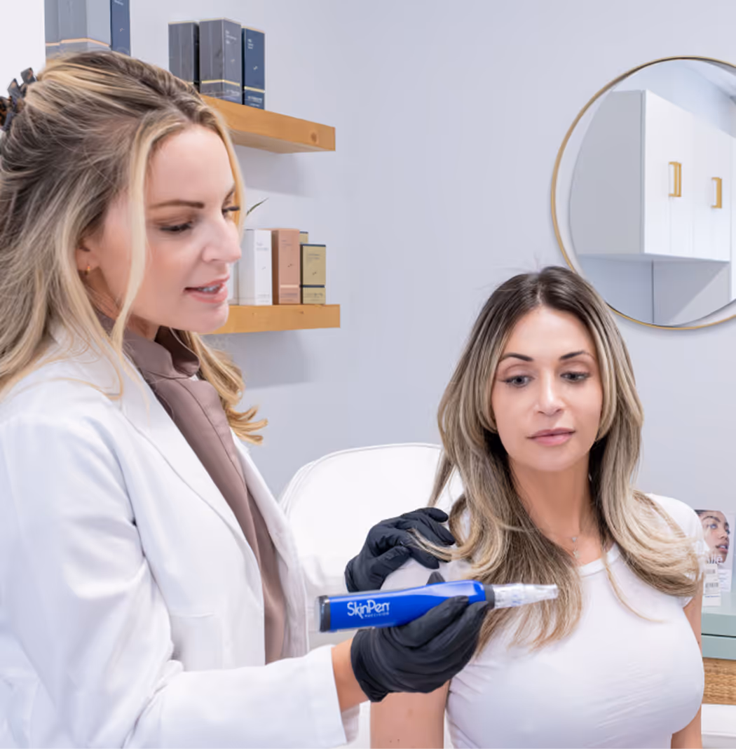 Woman in a white coat holding a SkinPen device near another woman’s shoulder in a clinic.