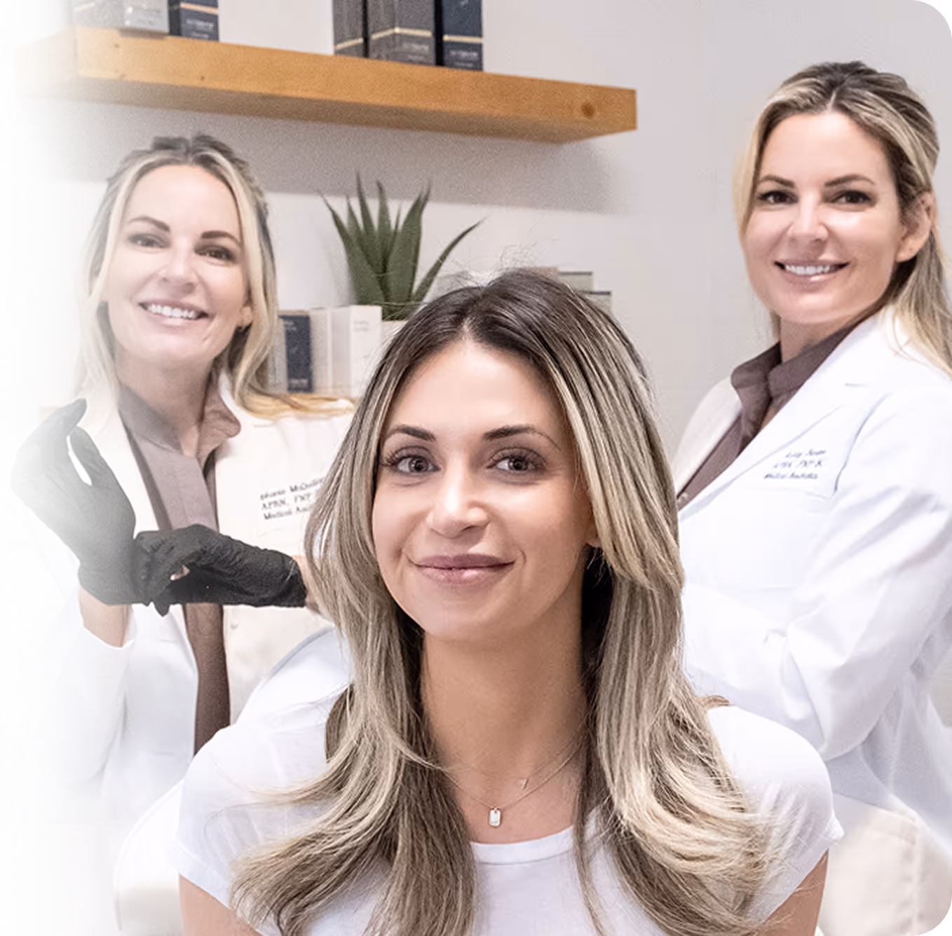 Smiling woman seated with two female medical professionals in white coats behind her.