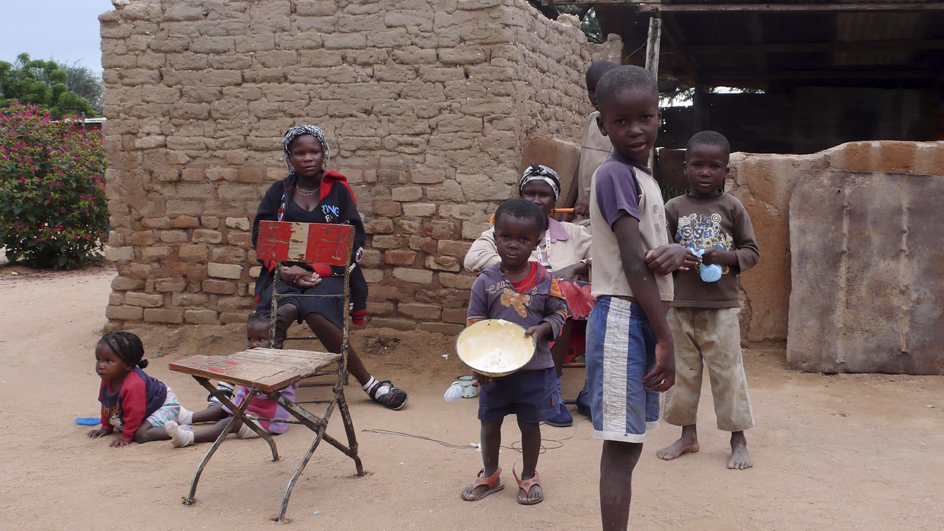 Gruppe afrikanischer Kinder und Frauen vor einer Lehmmauer in einem Dorf.