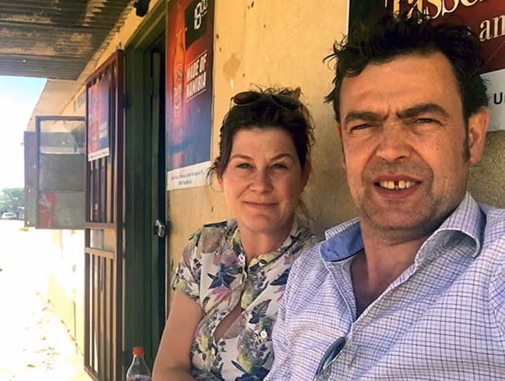 Mann und Frau sitzen zusammen vor einem Gebäude mit Plakaten an der Wand.