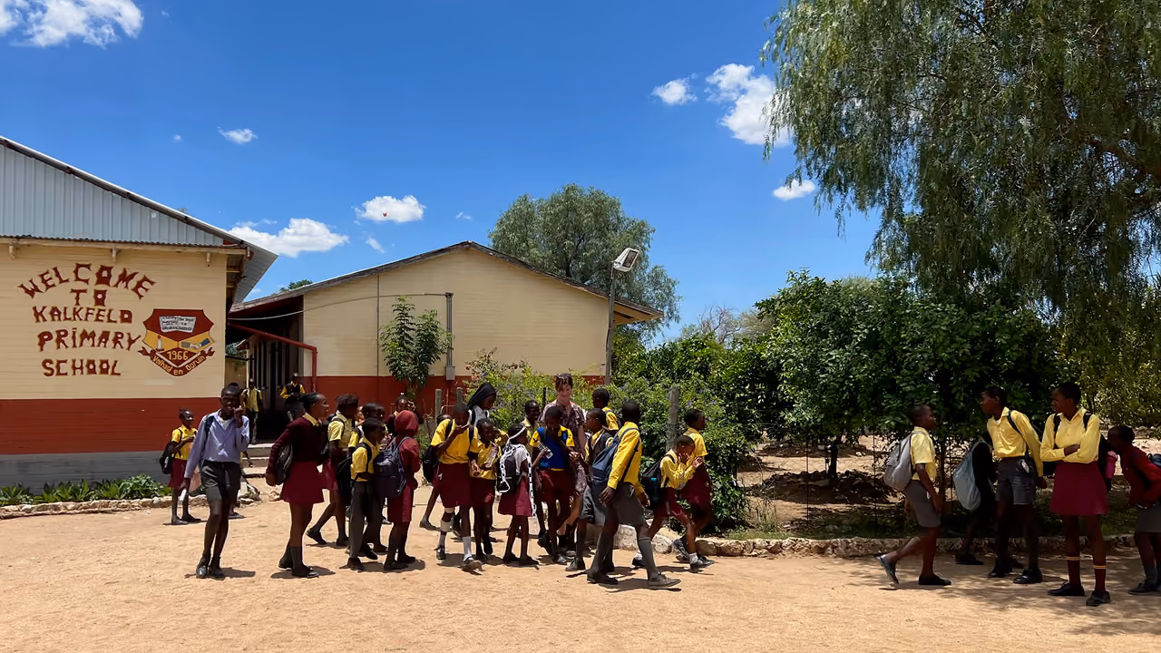 Schulkindern in gelben Hemden und roten Röcken oder Hosen auf dem Schulhof vor Kalkfeld Grundschule.
