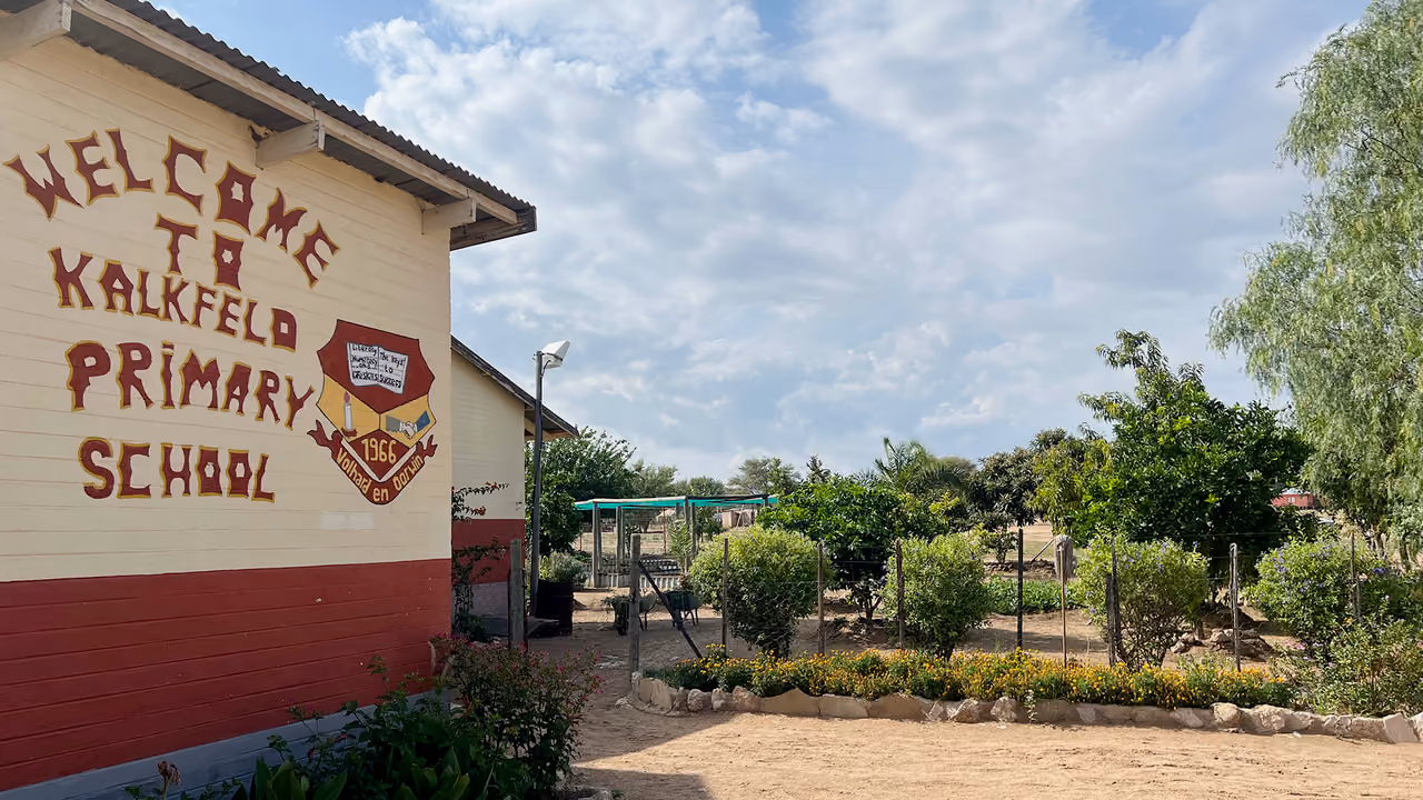 Außenansicht von Kalkfeld-Grundschule mit Garten, Zaun und bewölktem Himmel.