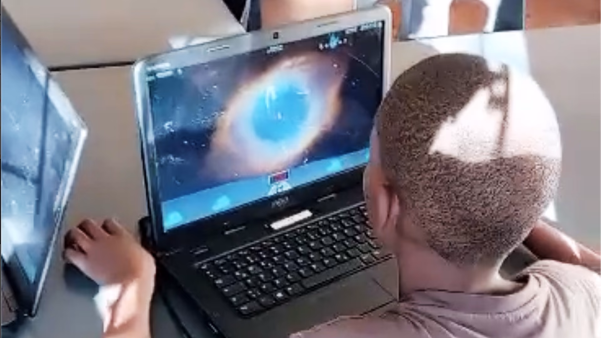 Junge spielt Computerspiel mit Weltraummotiv an einem Laptop in einem Klassenzimmer.