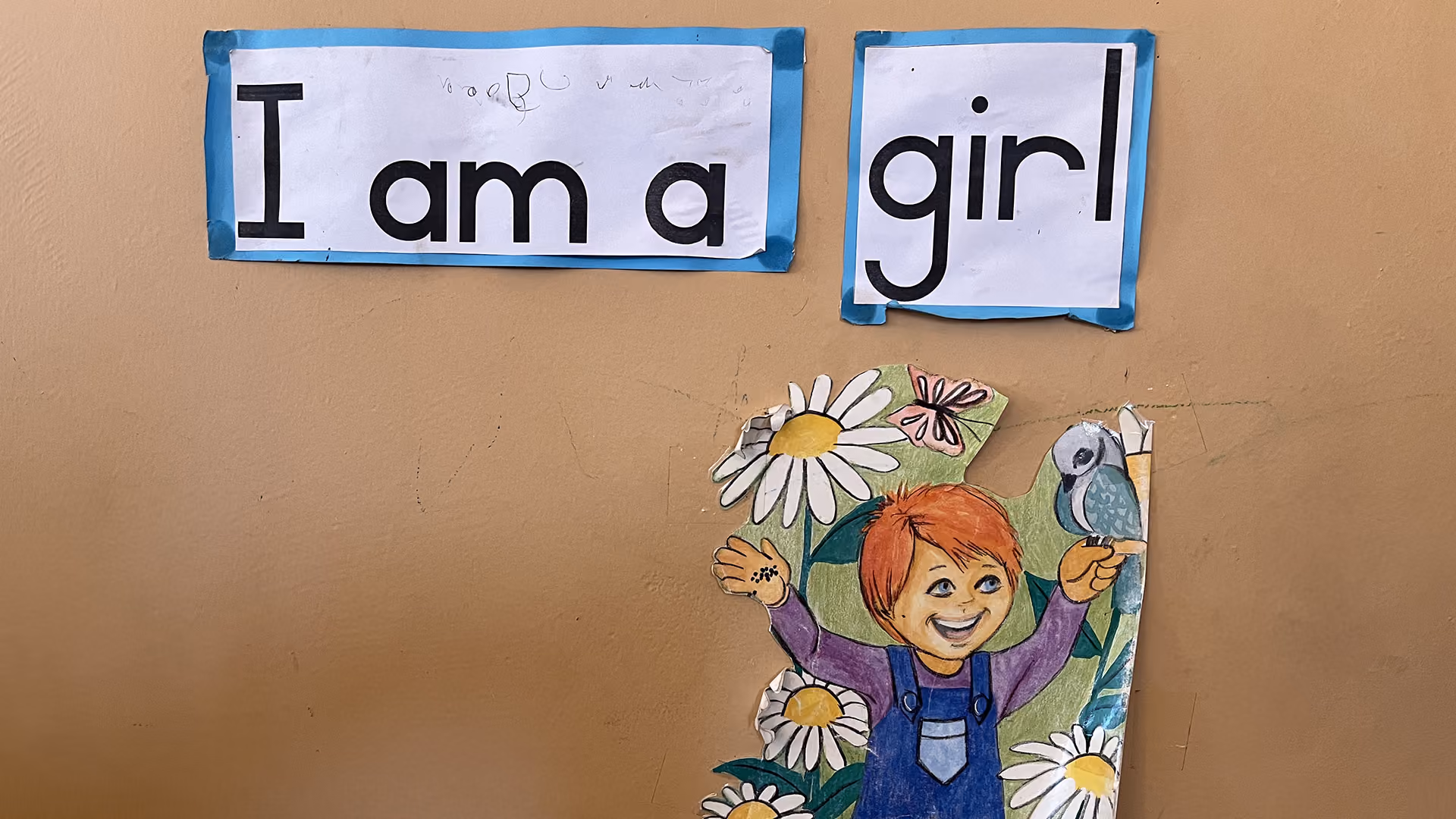 Kinderzeichnung eines rothaarigen Mädchens mit Blumen und Vogel unter Text 'I am a girl'.
