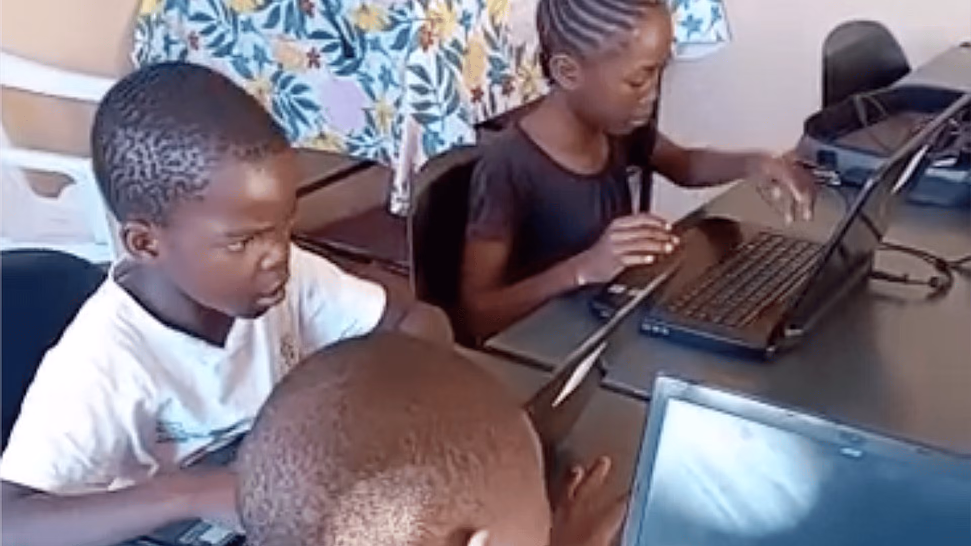 Drei Kinder arbeiten konzentriert an Laptops an einem Tisch in einem Klassenraum.
