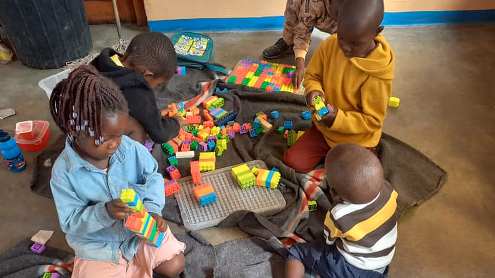 Kinder sitzen auf dem Boden und spielen mit bunten Bauklötzen in einem Innenraum.