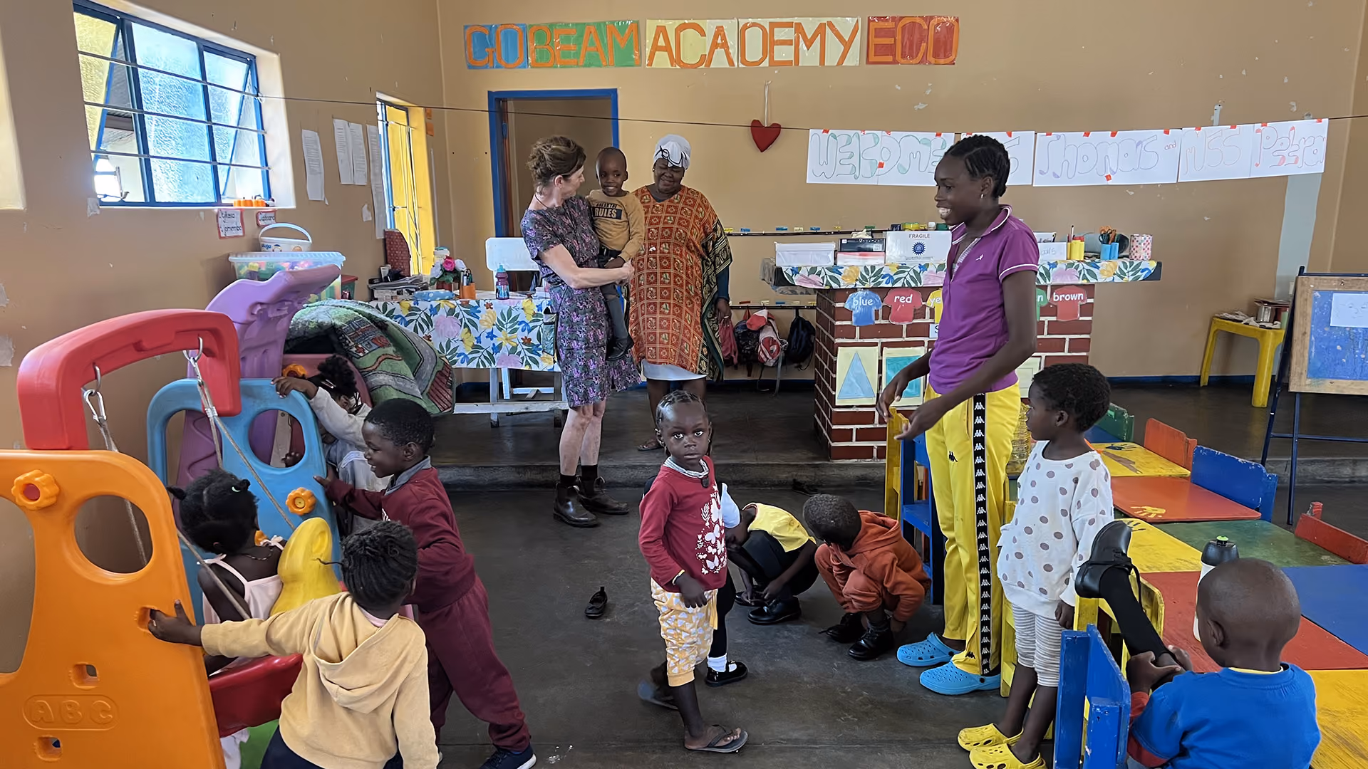 Lehrerin und Kinder spielen in einem farbenfrohen Klassenzimmer der GoBeam Academy Eco.