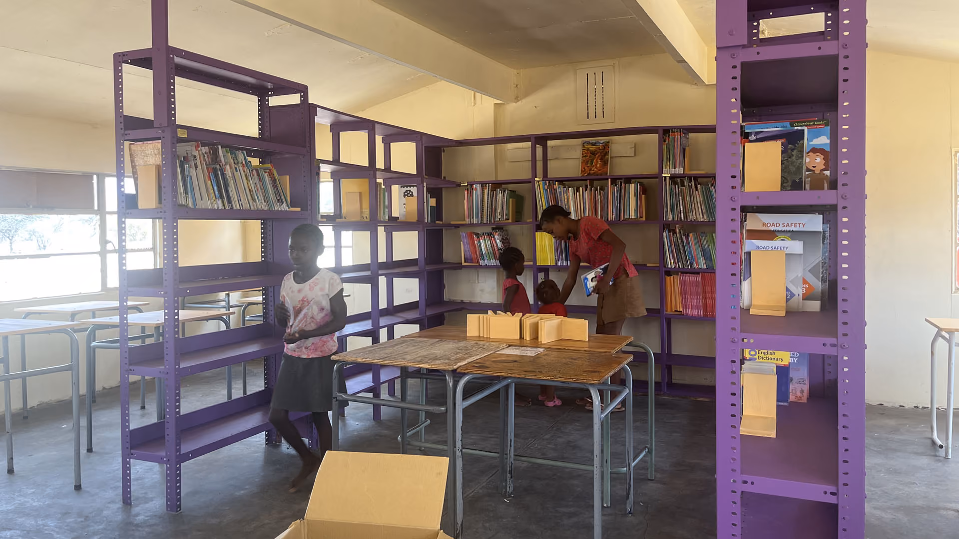 Kinder in einer Schule stehen in einer Bibliothek mit violetten Regalen und Büchern.