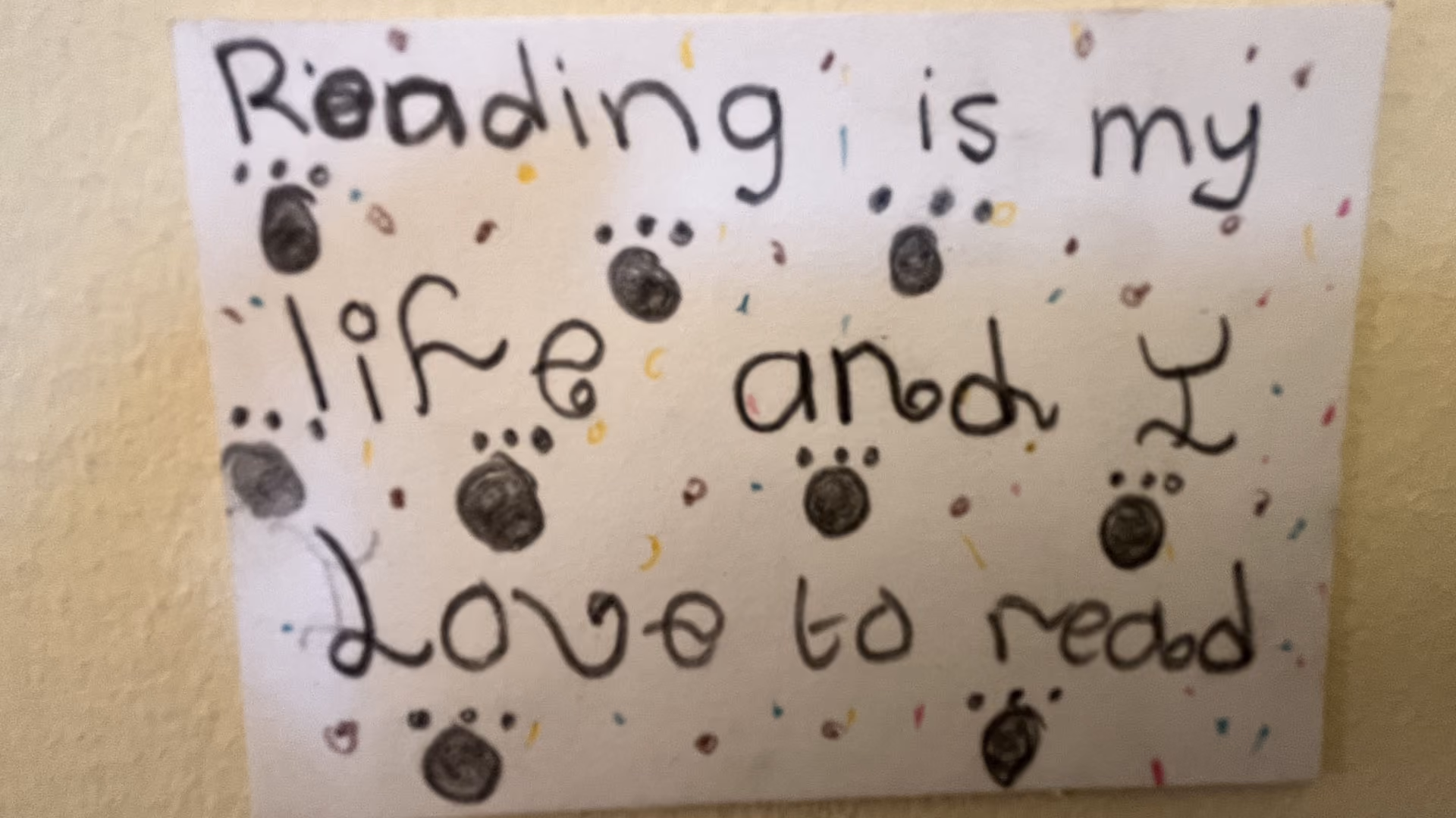 Handwritten sign with paw prints says reading is my life and I love to read.