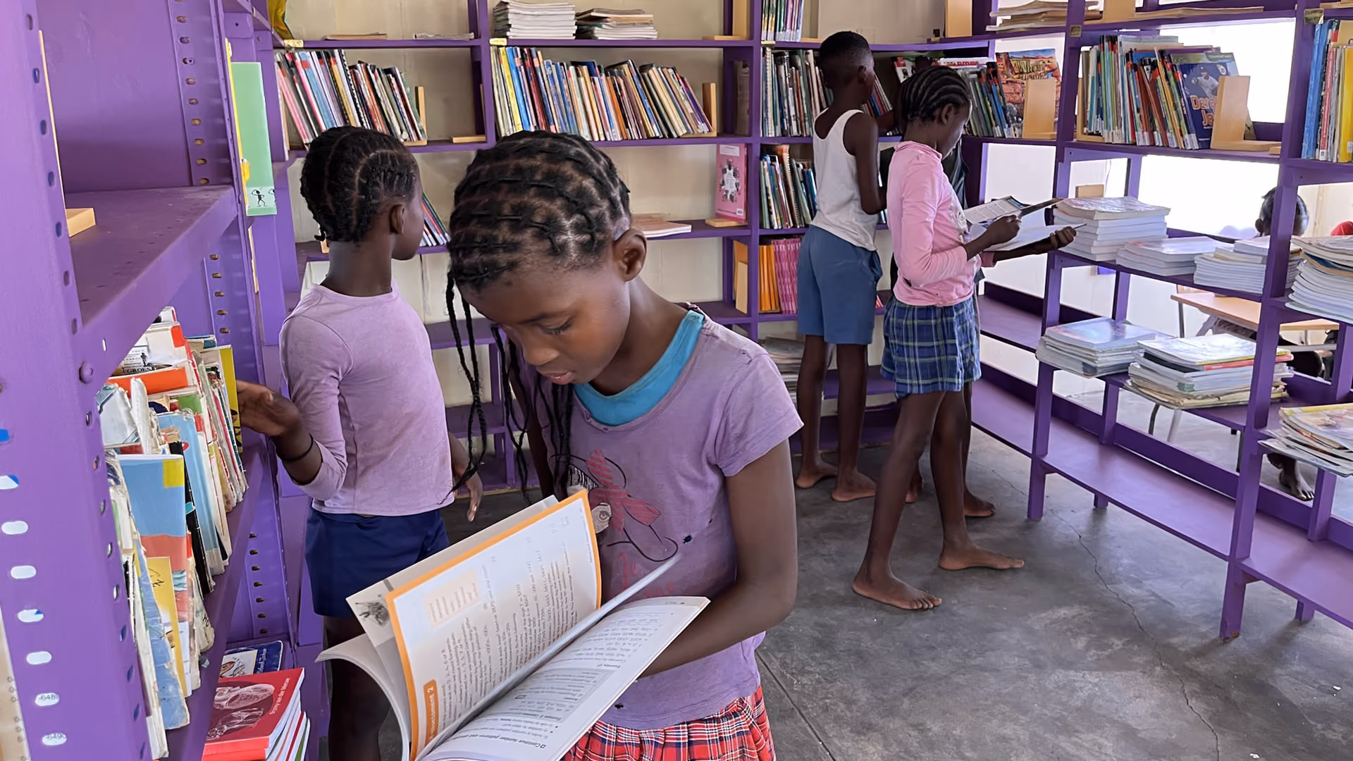 Kinder lesen und suchen Bücher in einer kleinen lilafarbenen Bibliothek mit Regalen.