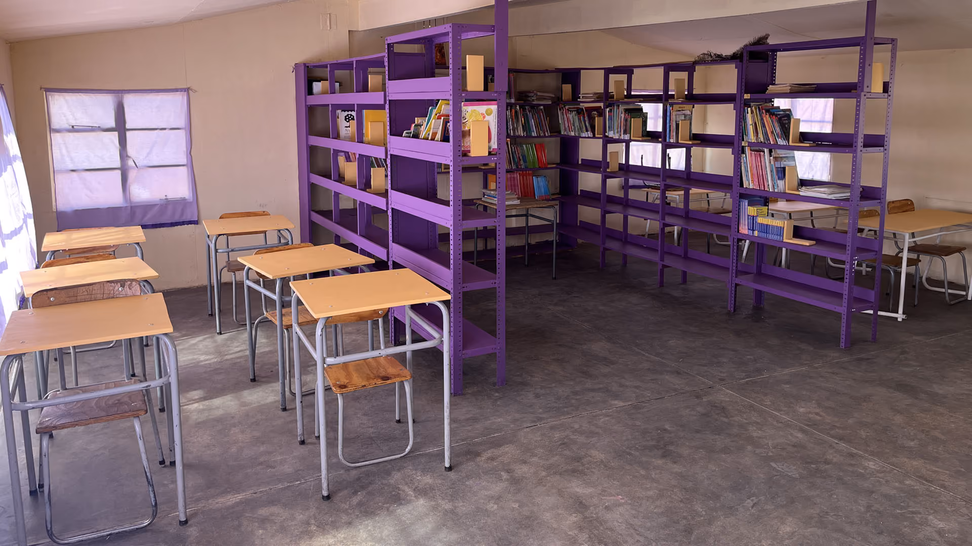 Klassenzimmer mit violetten Bücherregalen und Holzschultischen mit Metallbeinen.